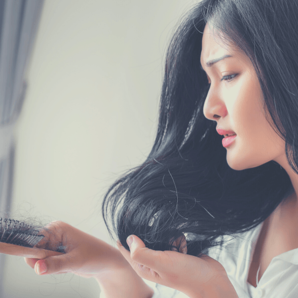 junge Frau mit schönen langen Haaren schaut auf eine Bürste mit ihren Haaren.