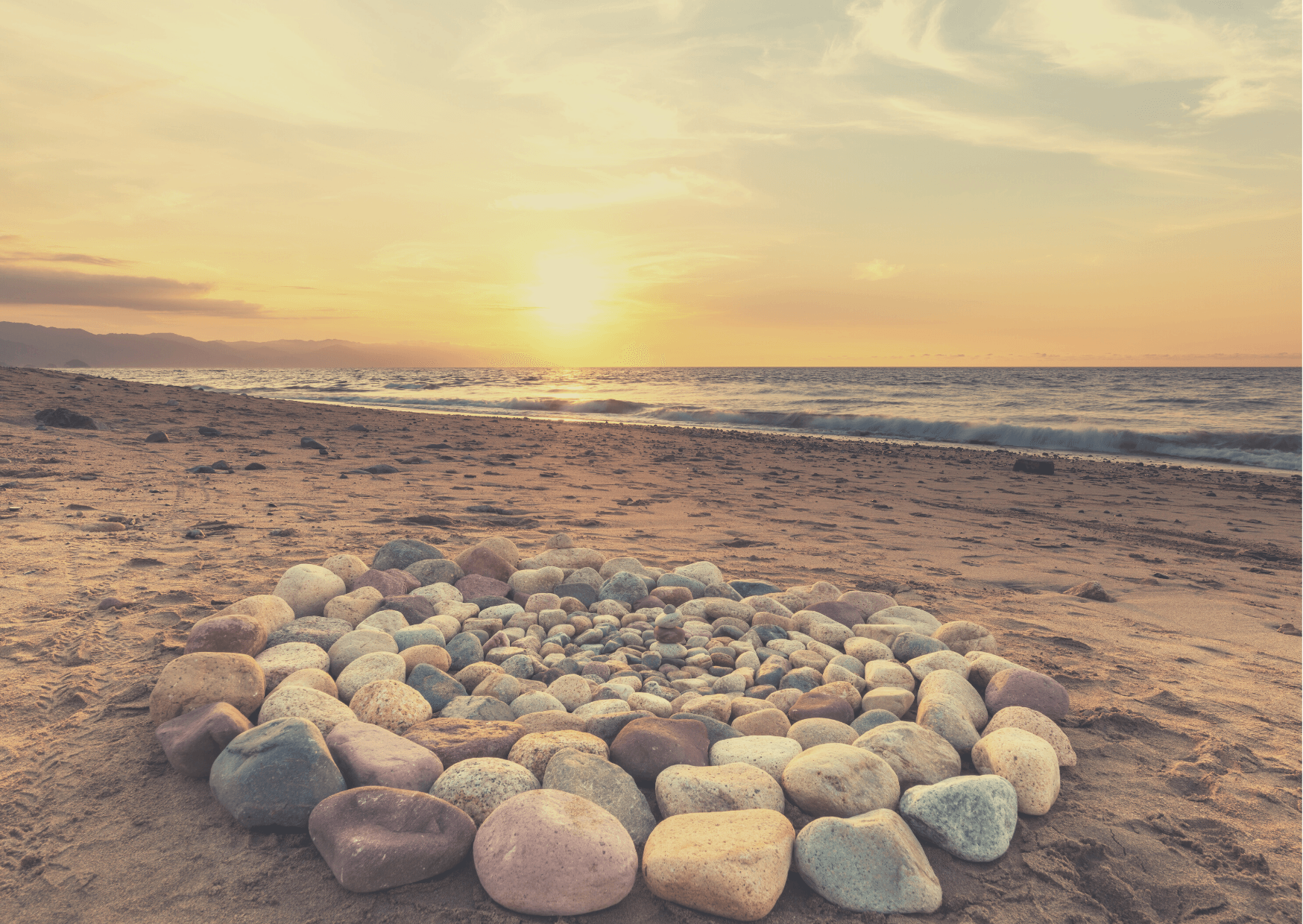 Angeordnete Steine liegen an einem Strand während die Sonne untergeht